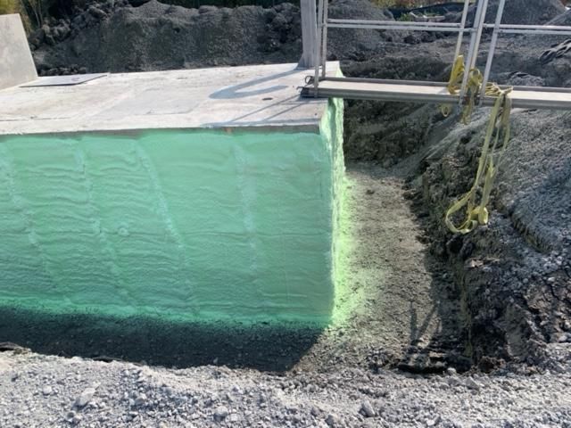 Isolation en mousse verte sur une structure en béton, avec une tranchée remplie de gravier à côté.