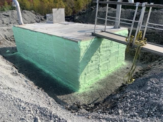 Structure en béton isolée verte en excavation avec passerelle métallique.