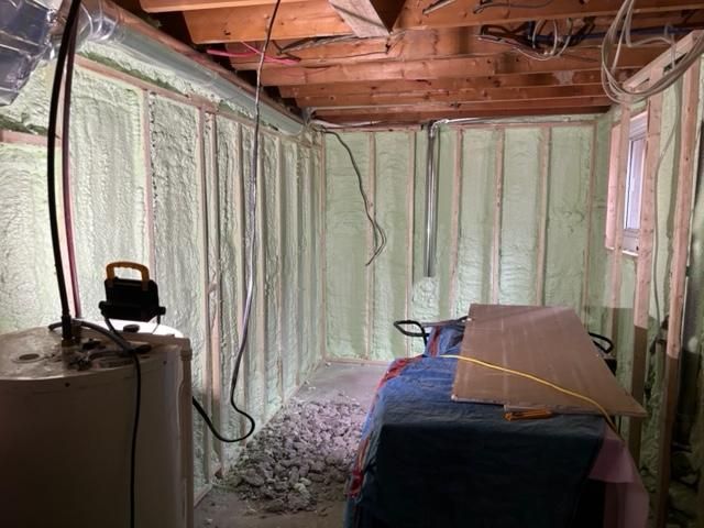 Sous-sol avec isolation en mousse projetée sur les murs. Fils électriques, chauffe-eau et débris visibles.