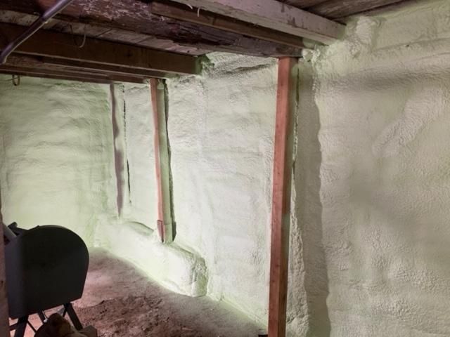 Murs du sous-sol isolés avec de la mousse projetée vert clair. Poutres et poteaux de soutien en bois visibles.