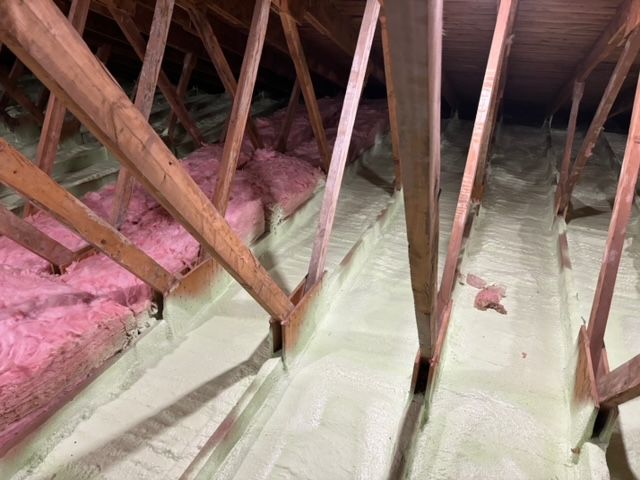 Grenier avec chevrons en bois, isolation en fibre de verre rose et isolation en mousse pulvérisée verte.