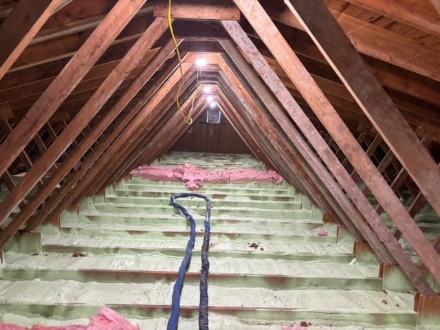 Intérieur du grenier avec isolation en mousse pulvérisée, fibre de verre rose et chevrons en bois.