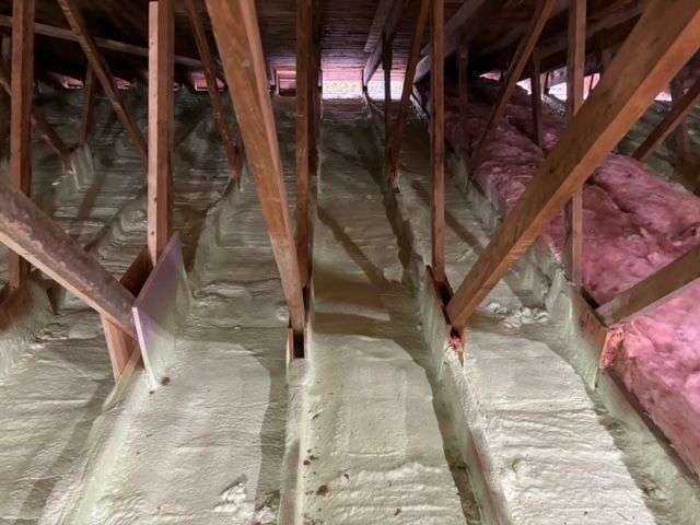 Combles avec isolation en mousse projetée entre les chevrons en bois; isolation rose sur le côté.