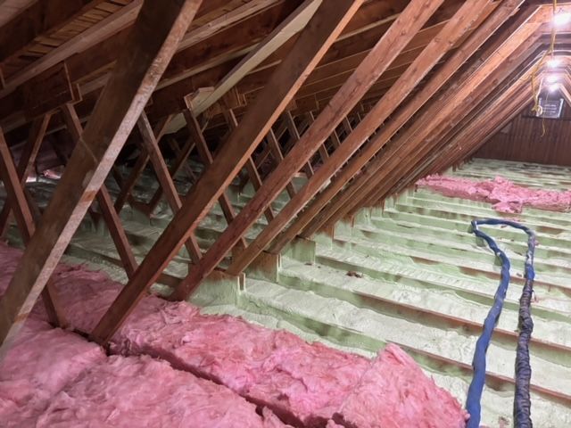 Intérieur des combles avec chevrons en bois et isolation rose au sol, et isolation verte dans les cavités.