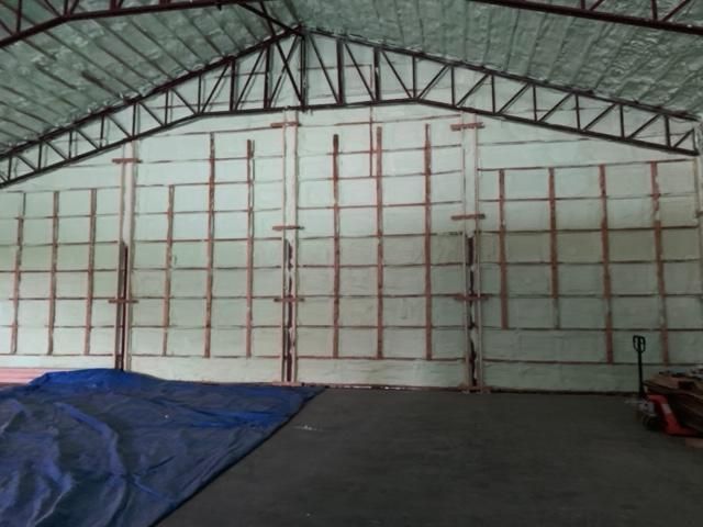 Intérieur d'un entrepôt, murs et plafond isolés avec poutres métalliques. Bâche bleue au sol.