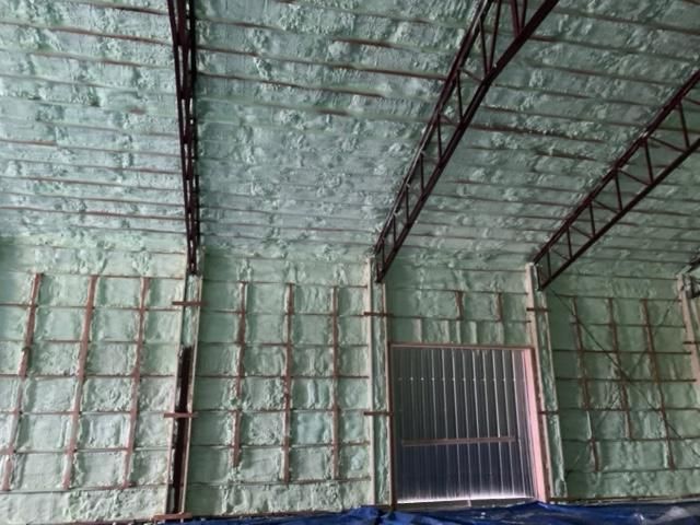 Isolation en mousse pulvérisée verte recouvrant la charpente métallique et les murs d'un bâtiment.