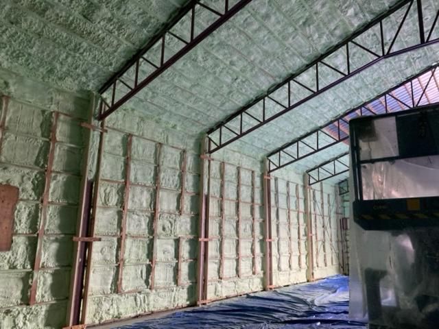 Intérieur d'un bâtiment avec isolation en mousse pulvérisée verte sur les murs et le plafond, poutres de support en métal.