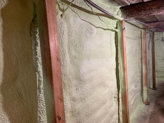 Mur de sous-sol avec ossature en bois, recouvert d'une isolation en mousse pulvérisée vert clair.