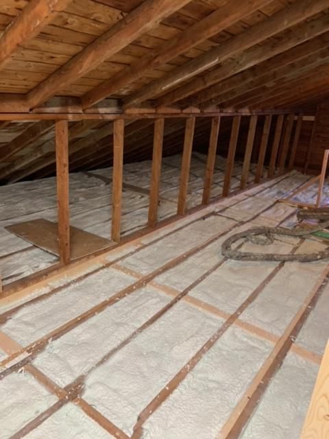 Combles avec poutres en bois et isolation. Isolation beige entre solives en bois, chevrons au-dessus.