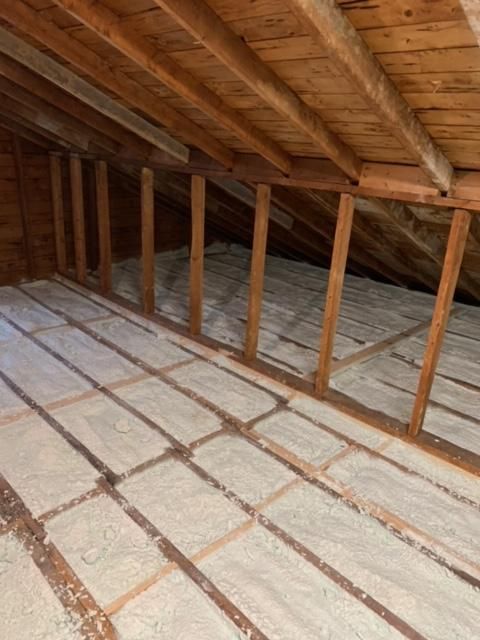 Intérieur mansardé avec poutres et chevrons en bois. Le sol est recouvert d'isolant.