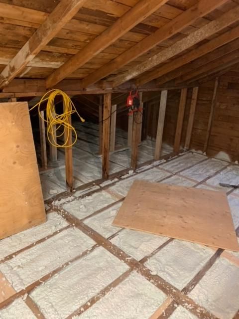 Intérieur du grenier avec charpente en bois apparente, isolation en mousse pulvérisée et rallonge jaune enroulée.