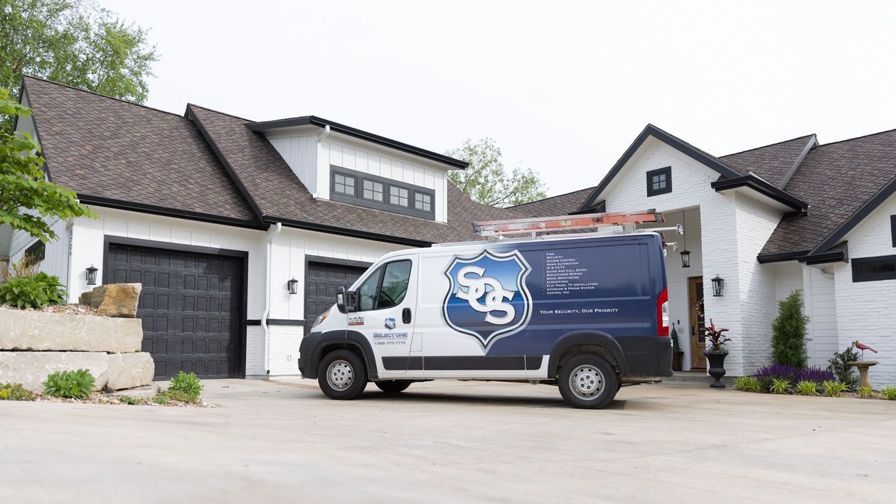 A blue service van with a shield logo parked in the driveway of a white, modern farmhouse-style home.