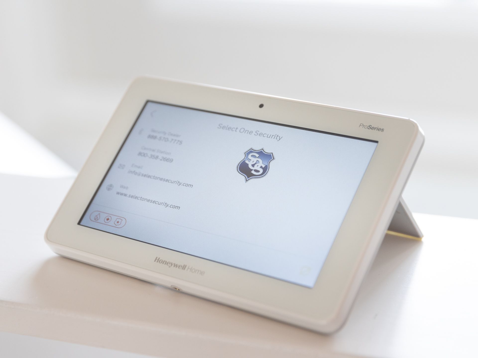 A white Honeywell home security touchscreen panel displaying system status, positioned on a light surface.