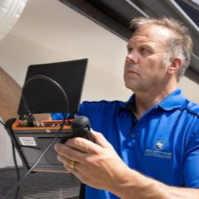 A person in a blue polo shirt holds a portable testing device with an attached screen while focusing on a task.