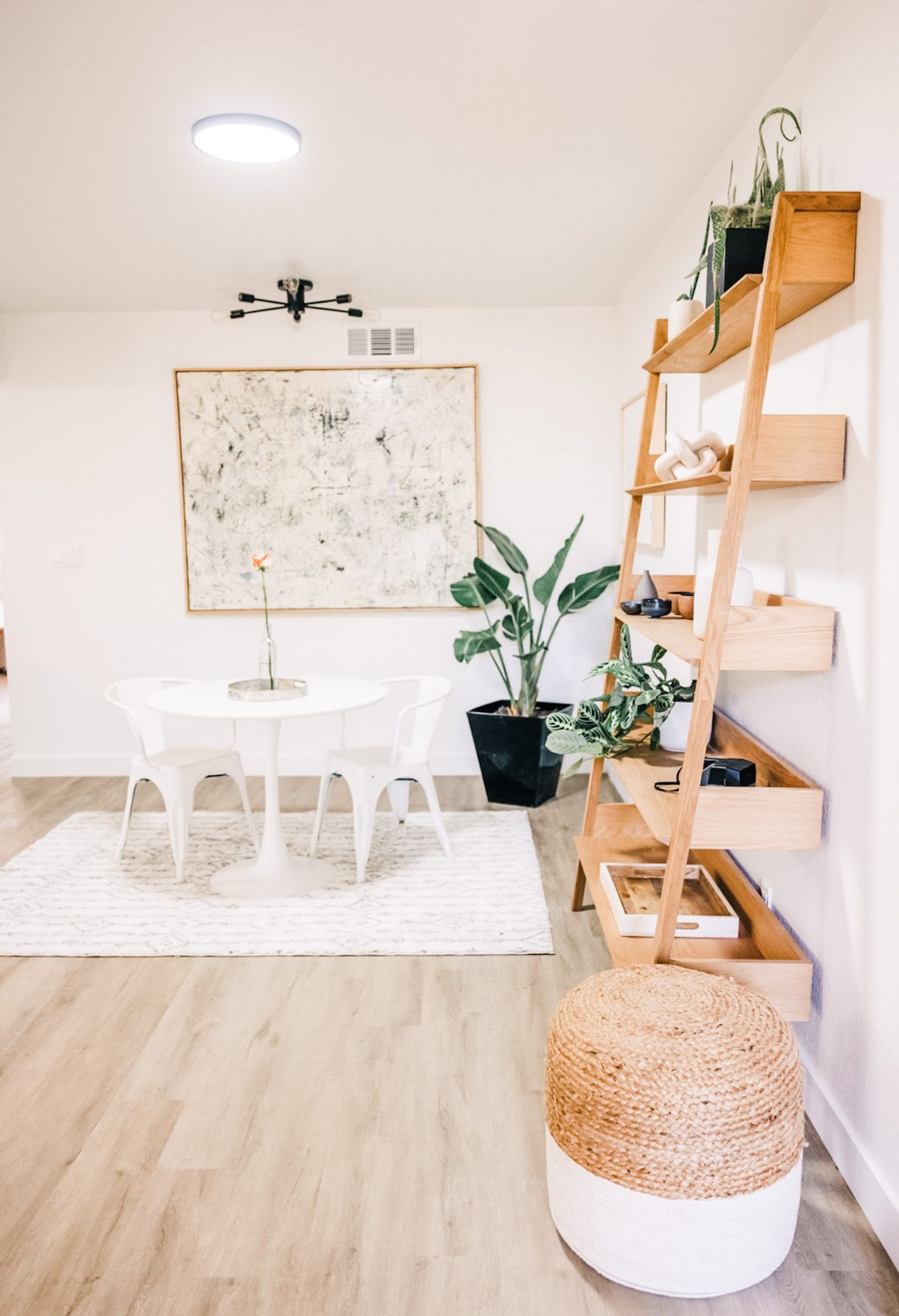 Bright dining area with white table, abstract art, and ladder shelf with plants.