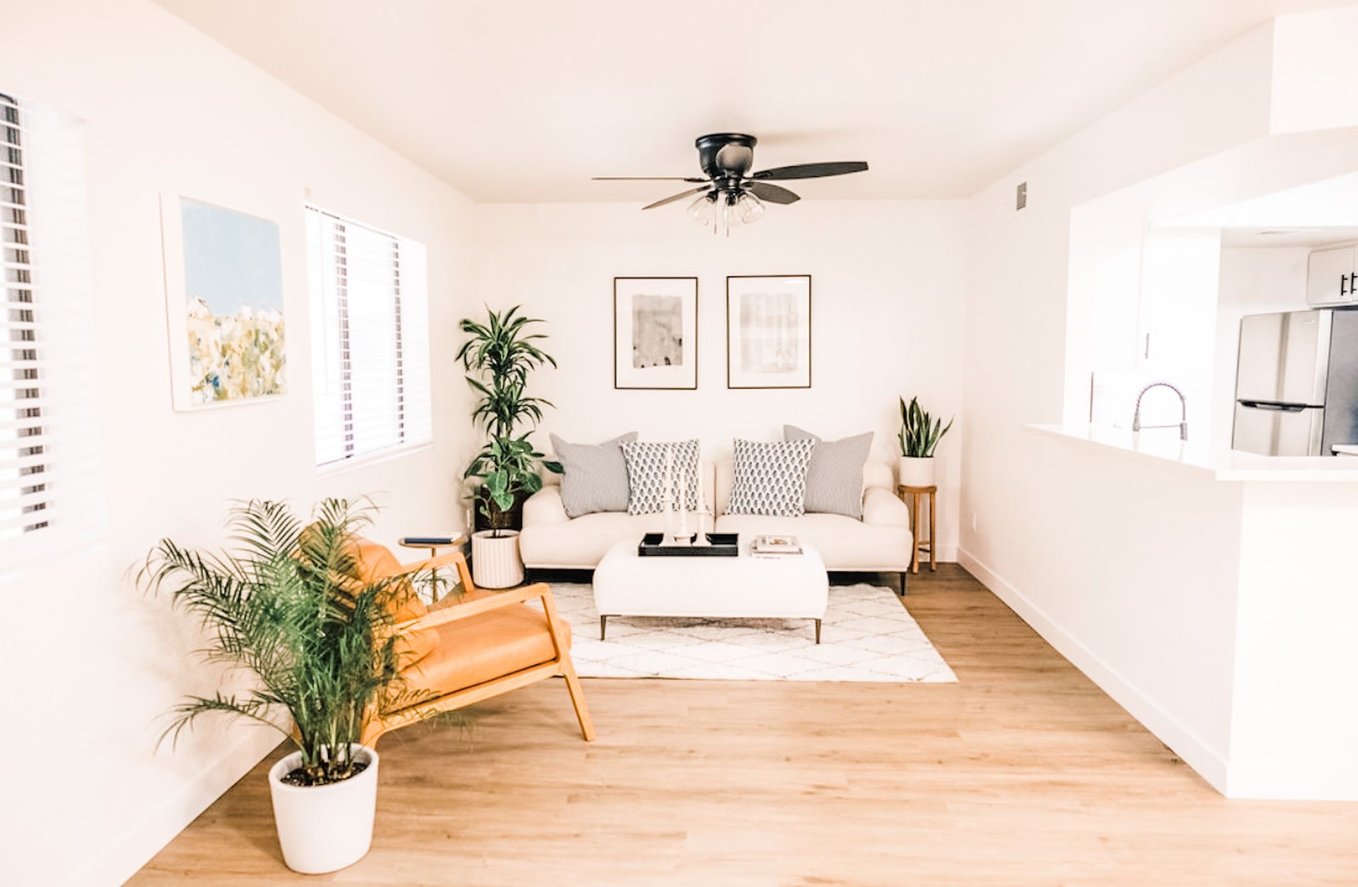 Living room: white walls, wood floors, light sofa, wicker chair, plants, and decor.