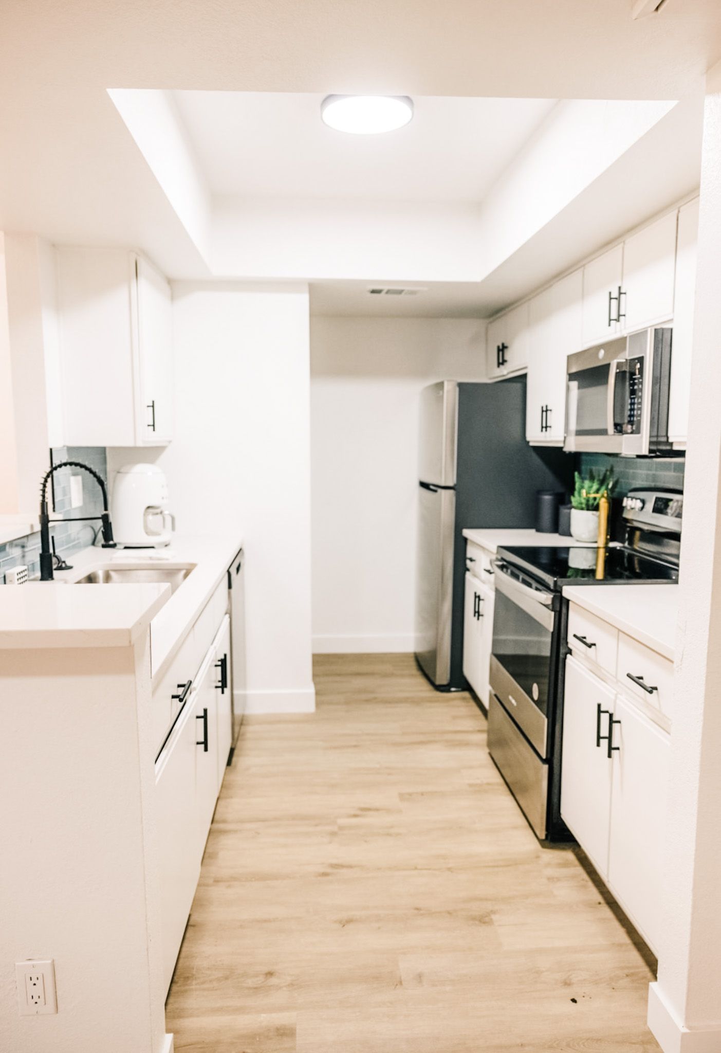 White kitchen with light wood floors, stainless steel appliances, and black hardware.