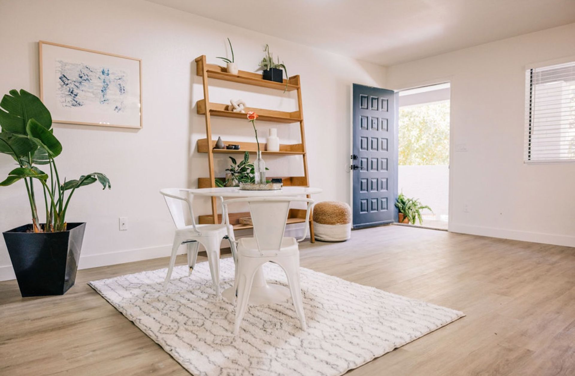 White dining room with table, chairs, rug, open door, and wooden shelf.