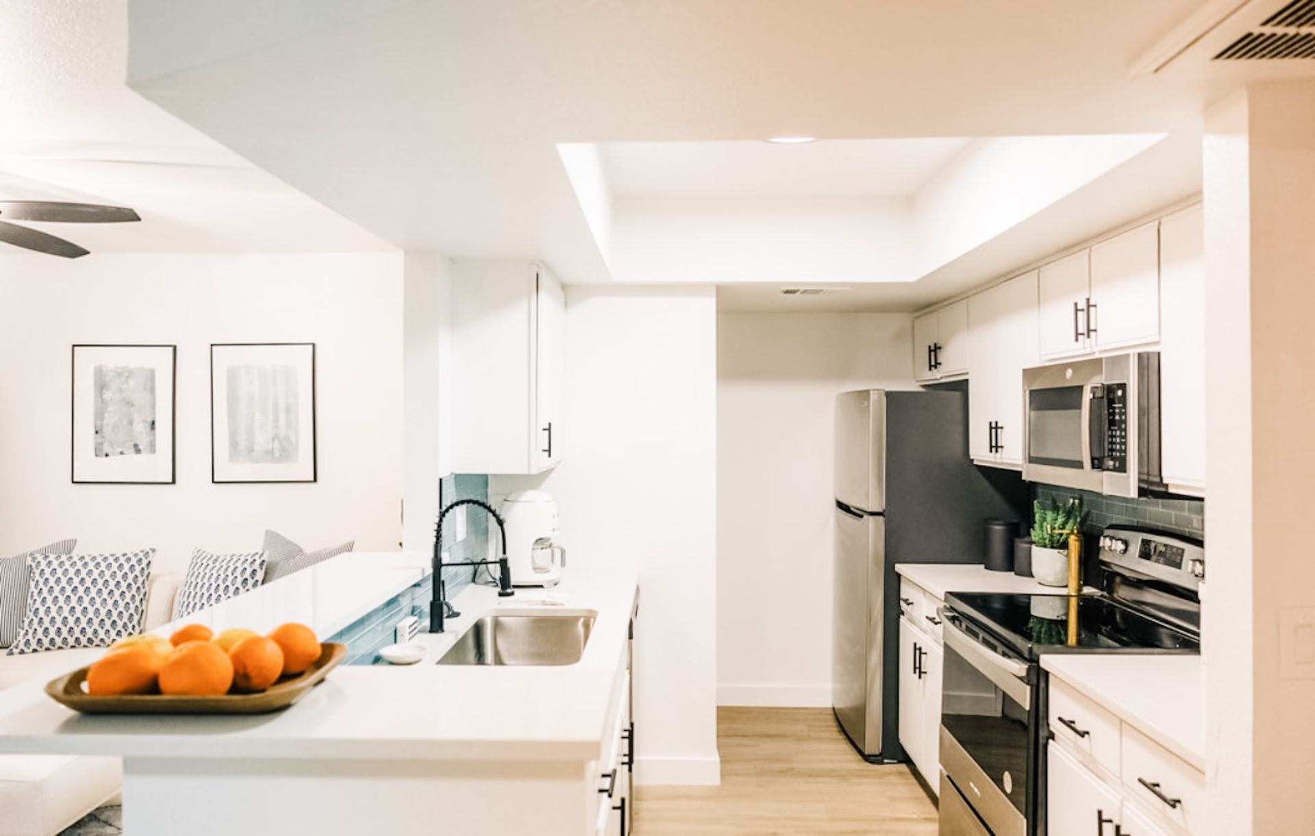 Modern kitchen with white cabinets, stainless steel appliances, and a bowl of oranges.