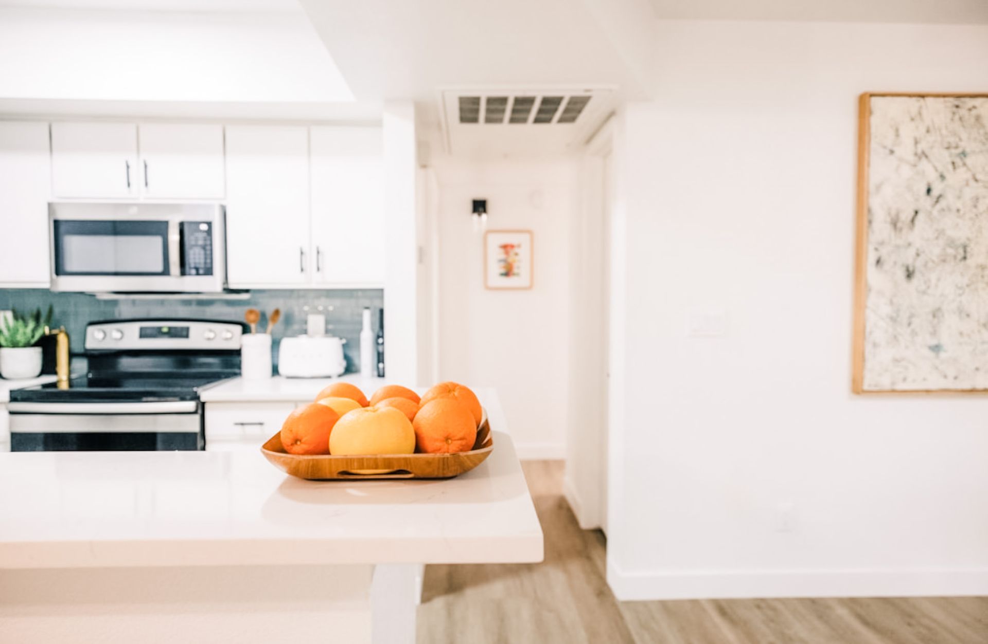 Kitchen with fruit bowl on island counter, white cabinets, stainless steel appliances, and artwork.