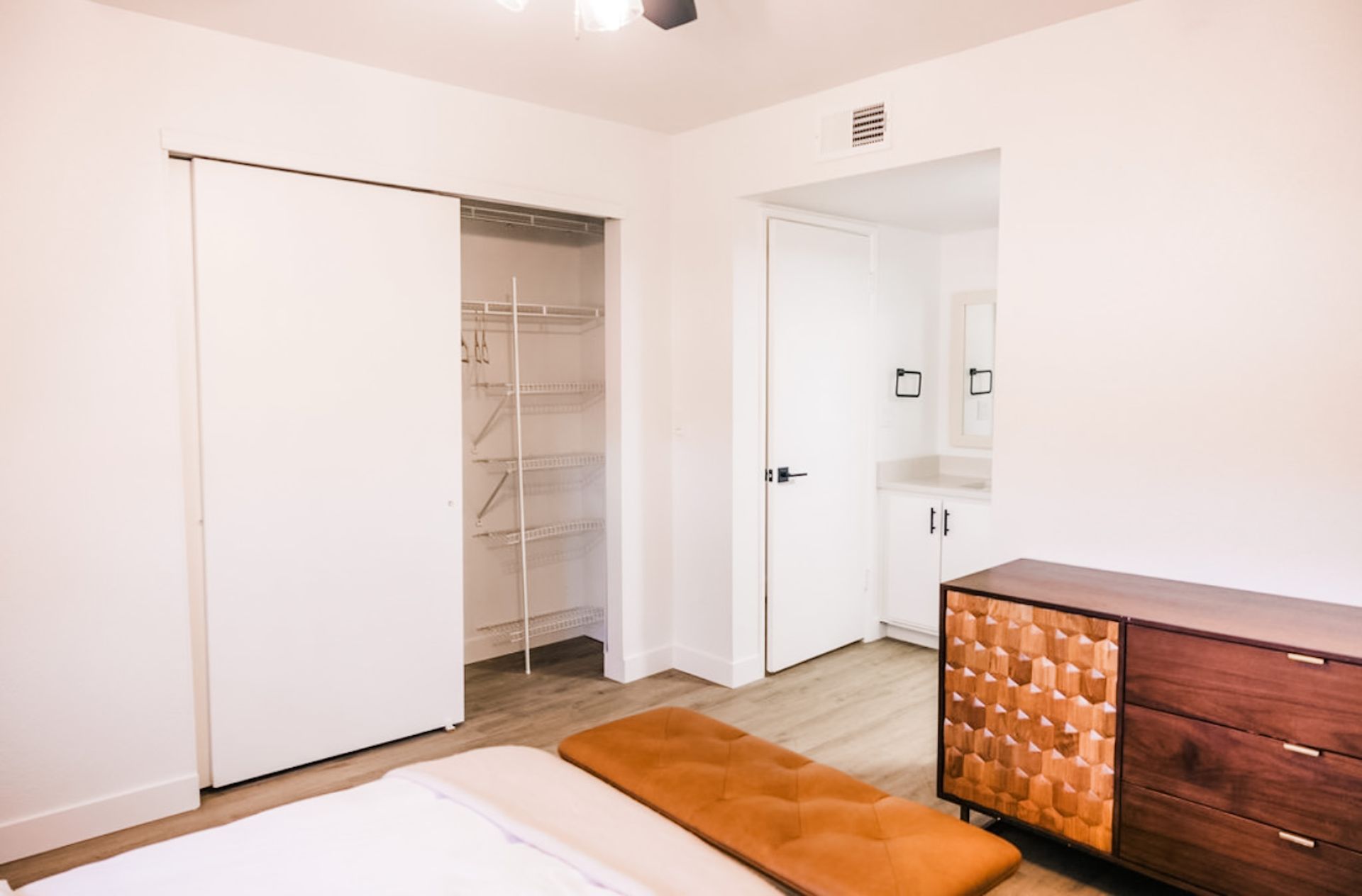 Bedroom with white walls, closet, and dresser; a bathroom door is visible.
