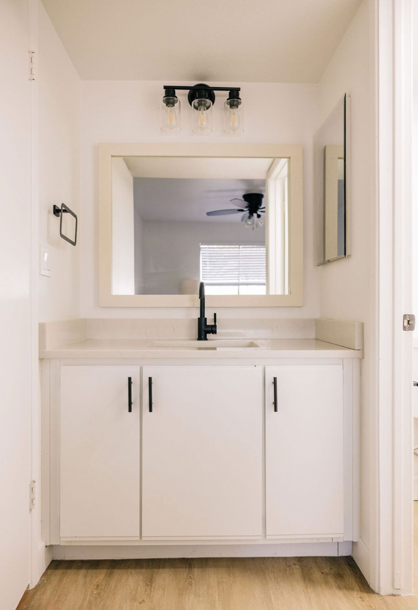 White bathroom with a vanity, mirror, and black fixtures.