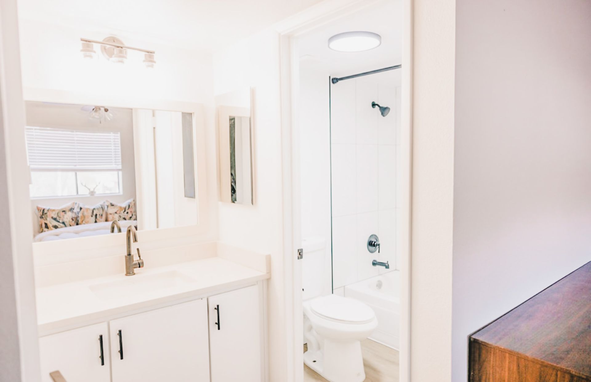 White bathroom with vanity, toilet, and shower visible through the doorway.