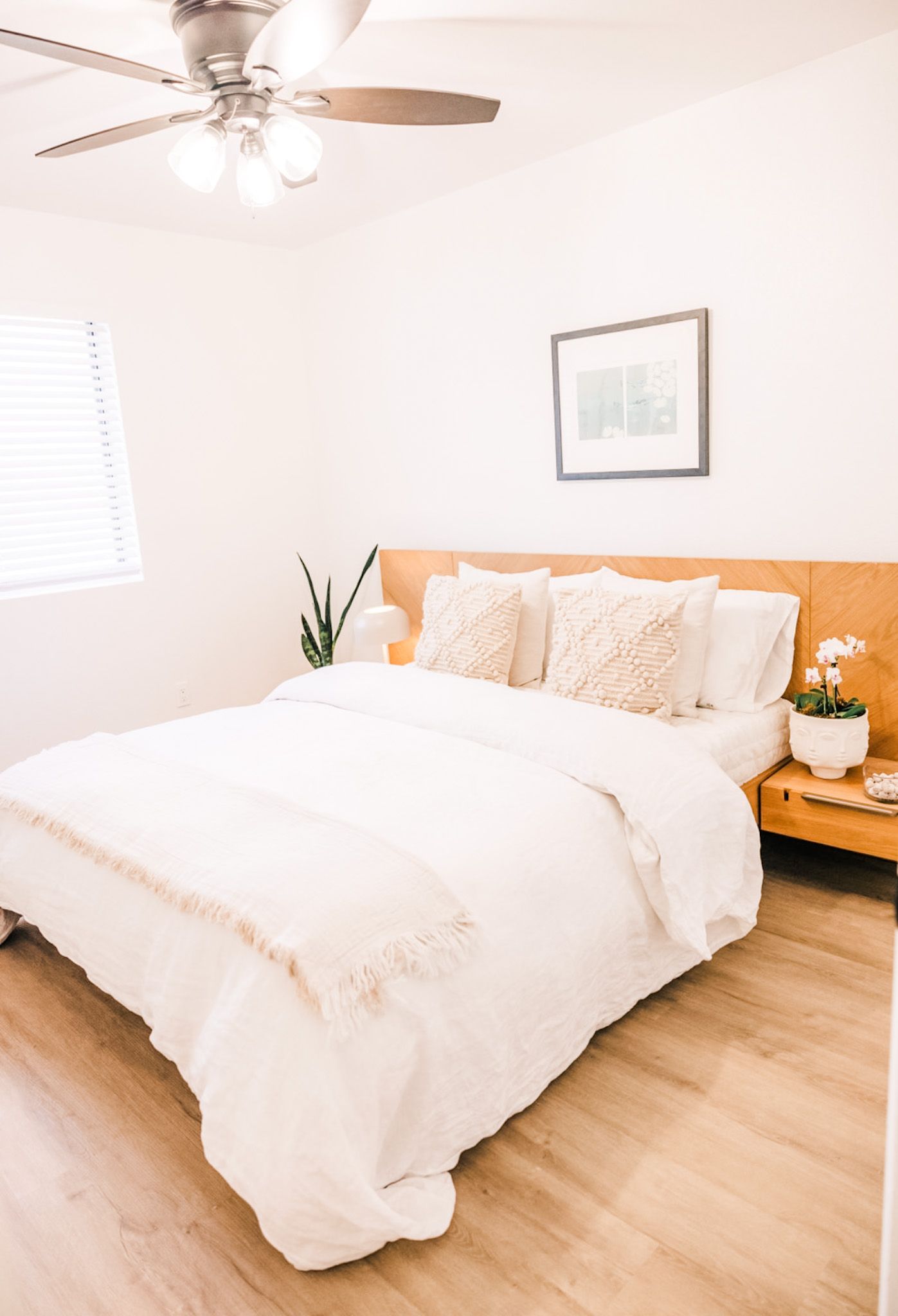 Bedroom with a bed, nightstand, and artwork; light-colored walls and wood floors.