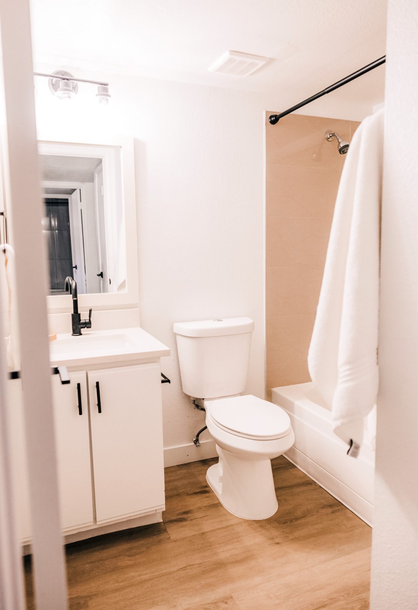 Bathroom with white vanity, toilet, and shower, light wood floor, and a white towel.