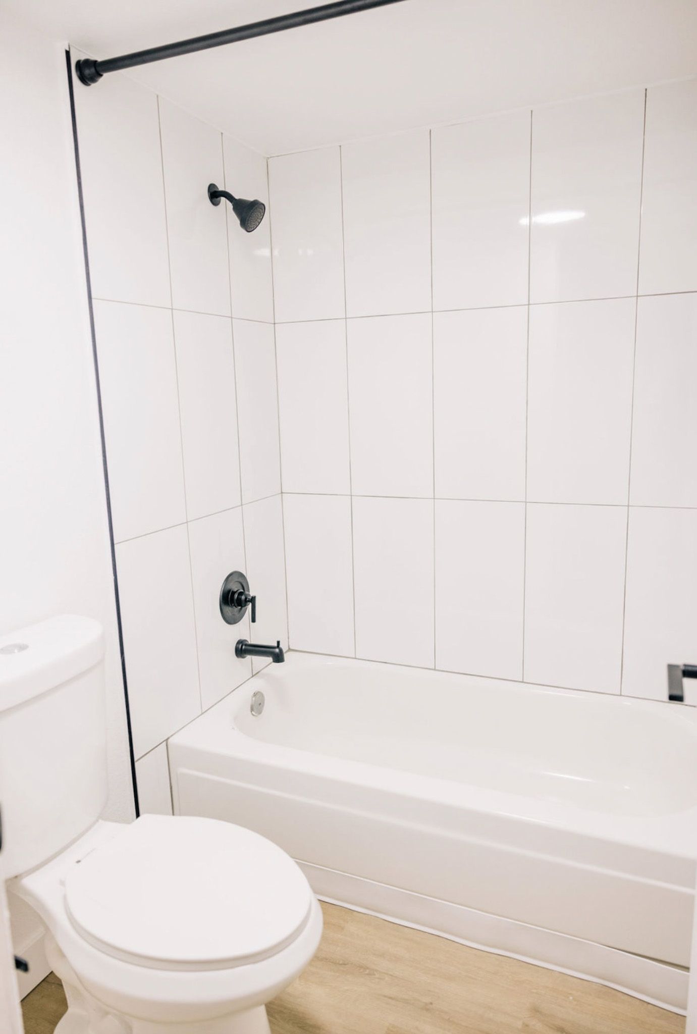 White bathroom with a toilet, bathtub, and showerhead; black fixtures and trim.