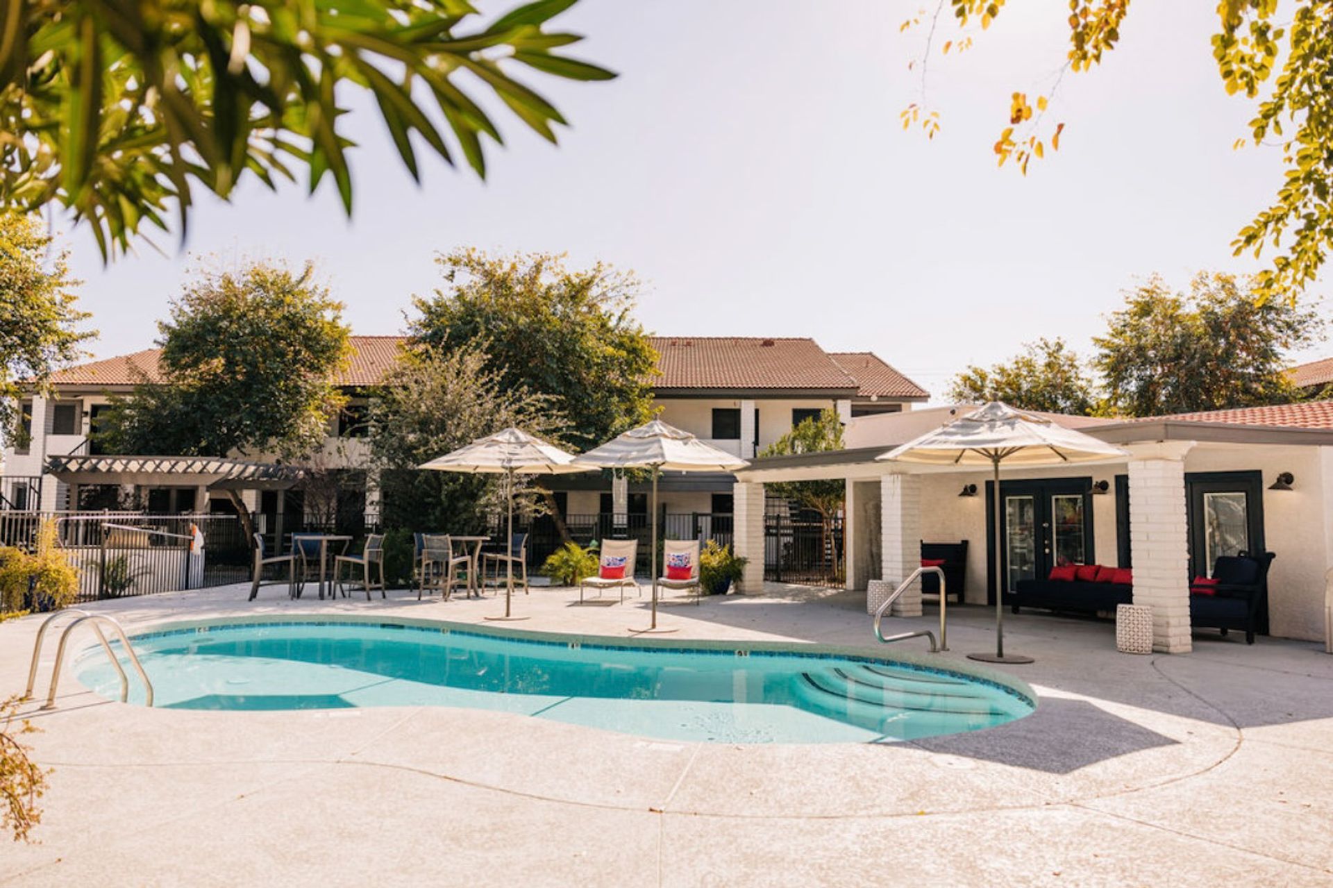 Pool with umbrellas, seating, and building in the background. Bright sunny day.