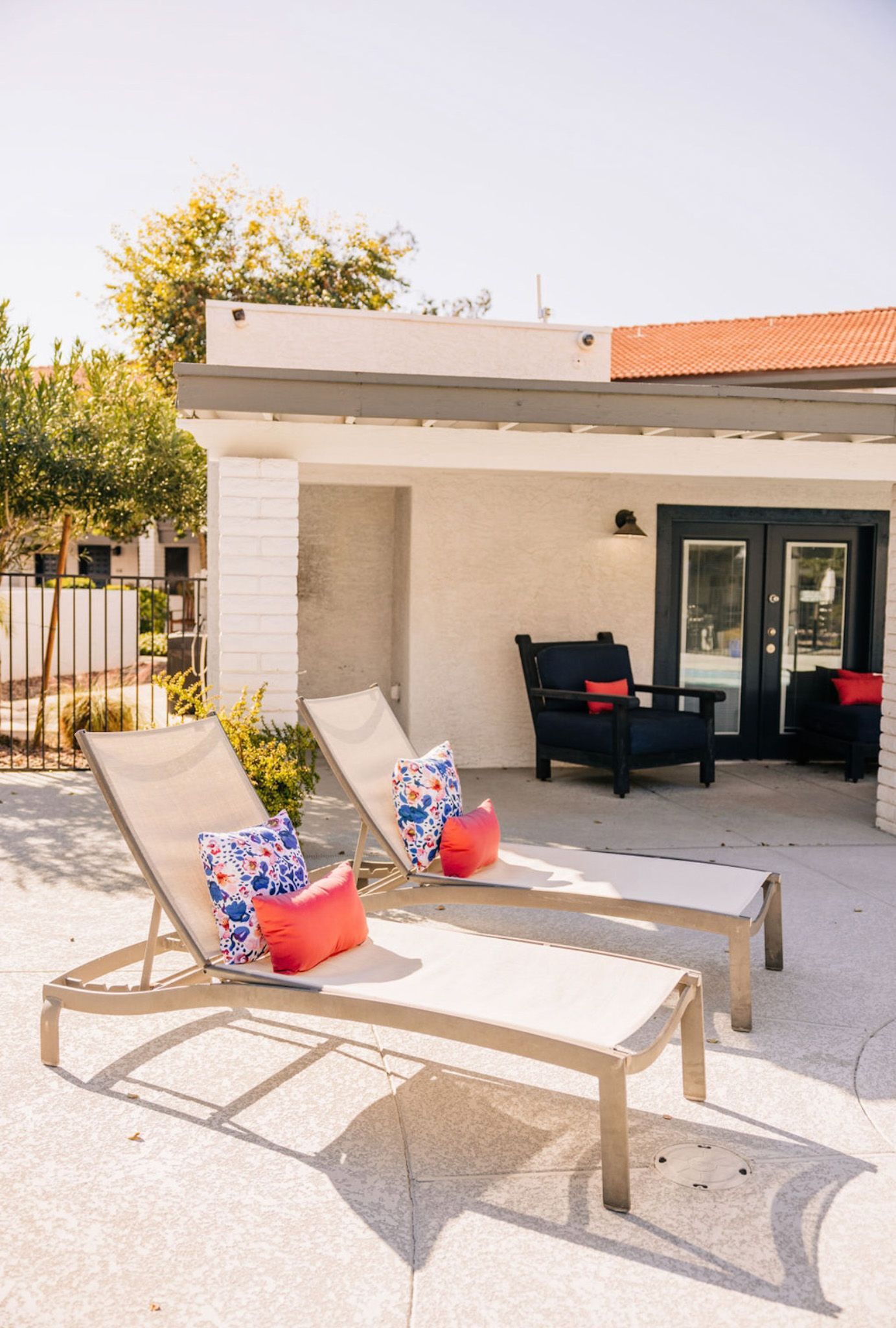Two lounge chairs with pillows near patio seating, under a building.