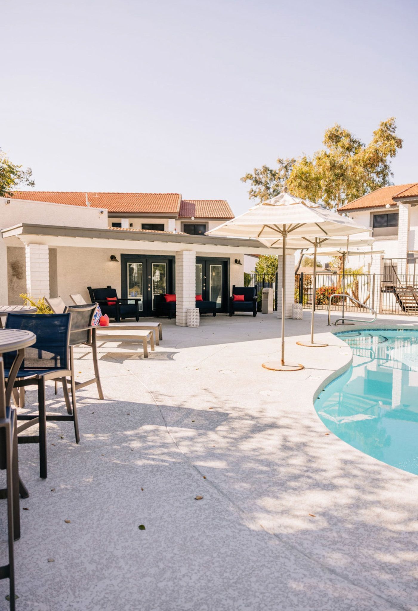 Poolside lounge area with white building, seating, and parasols.