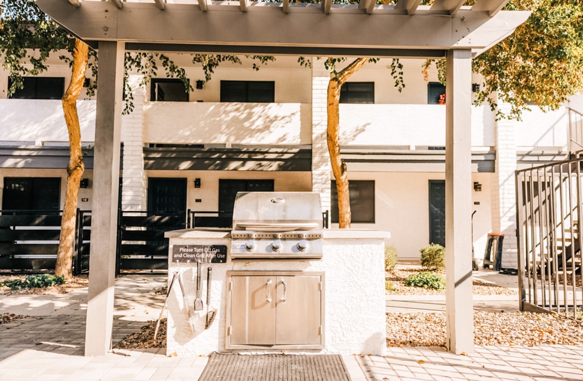 Outdoor grilling station in front of white townhouses with a pergola above.