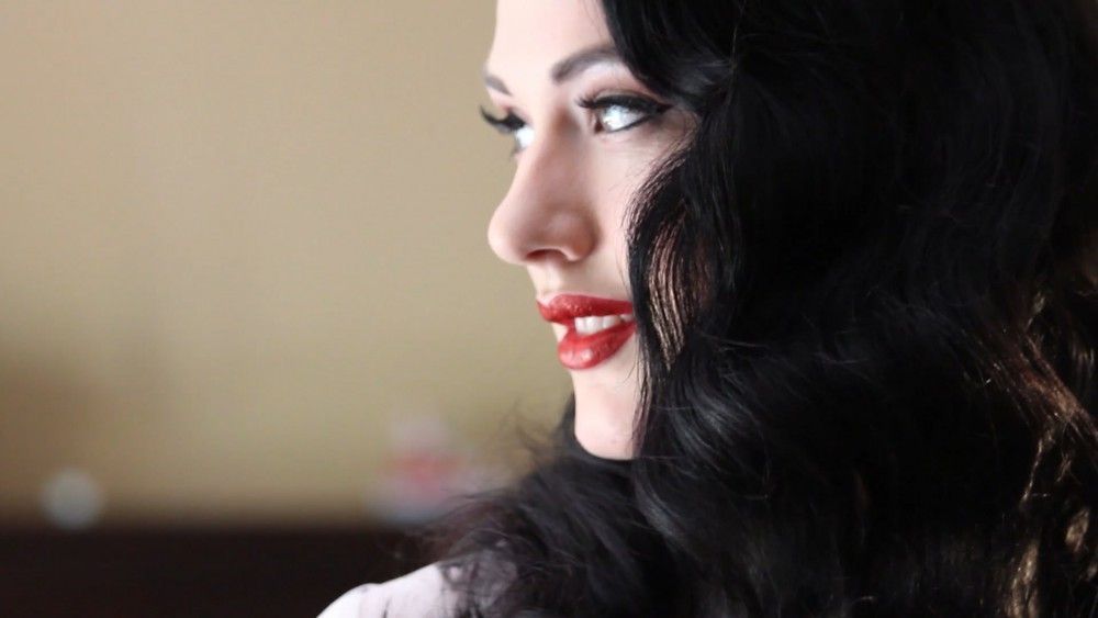 Woman with dark hair and red lipstick, looking over her shoulder, smiling.