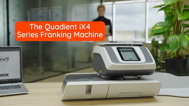 Quadient IX4 series franking machine on desk with laptop and person in background.
