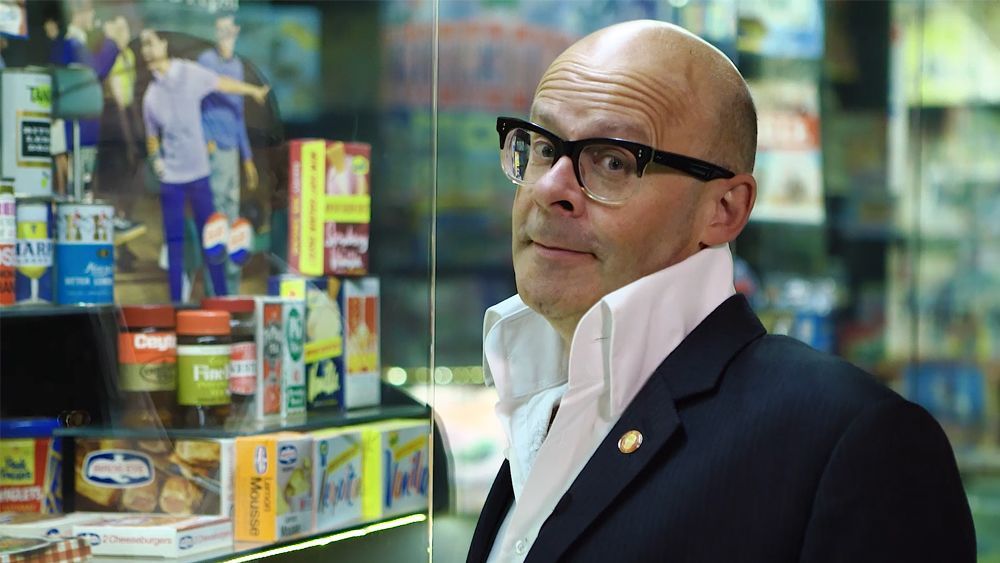 Man with glasses and white collar in front of a store display, looking to the side.