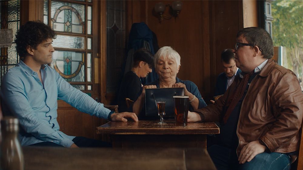 Three people in a pub looking at a tablet. Two men and a woman sit around a table with a pint.