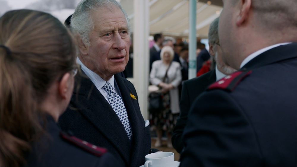 King Charles speaking with people in dark uniforms at an outdoor event.