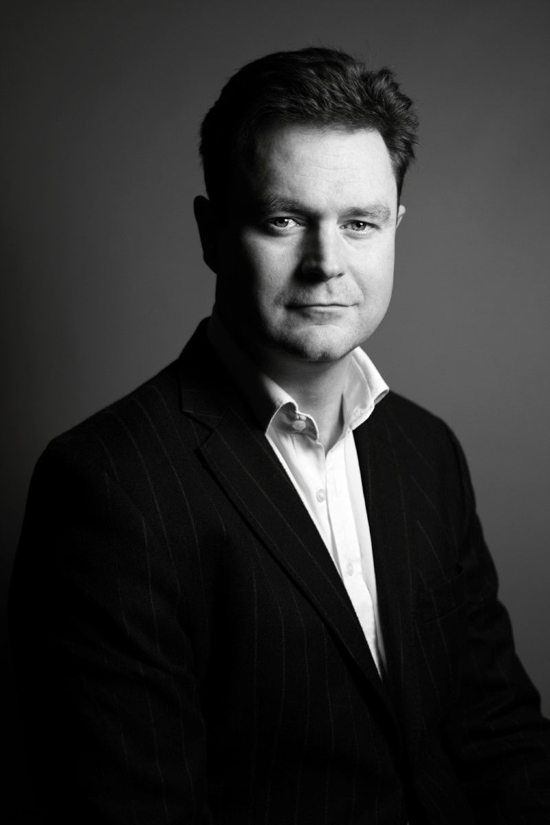 Jim Coogan in suit jacket, white shirt, looking forward with a neutral expression, black and white portrait.