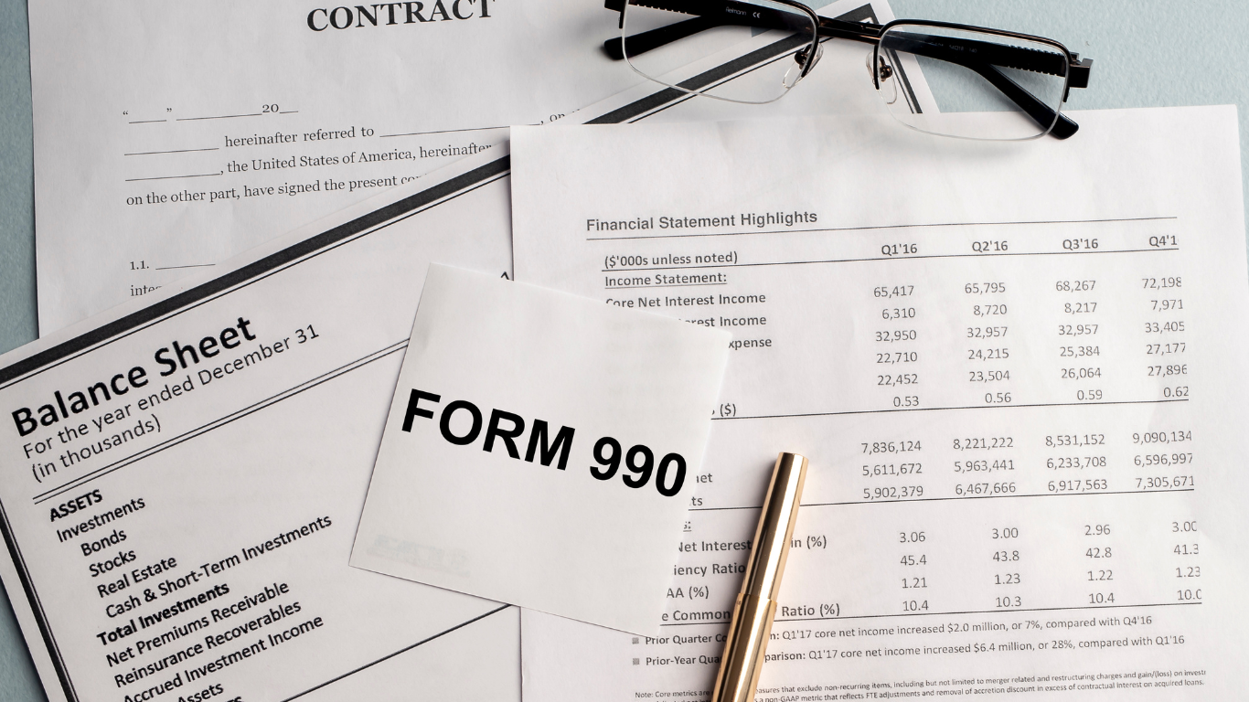 A form 990 is sitting on top of a balance sheet