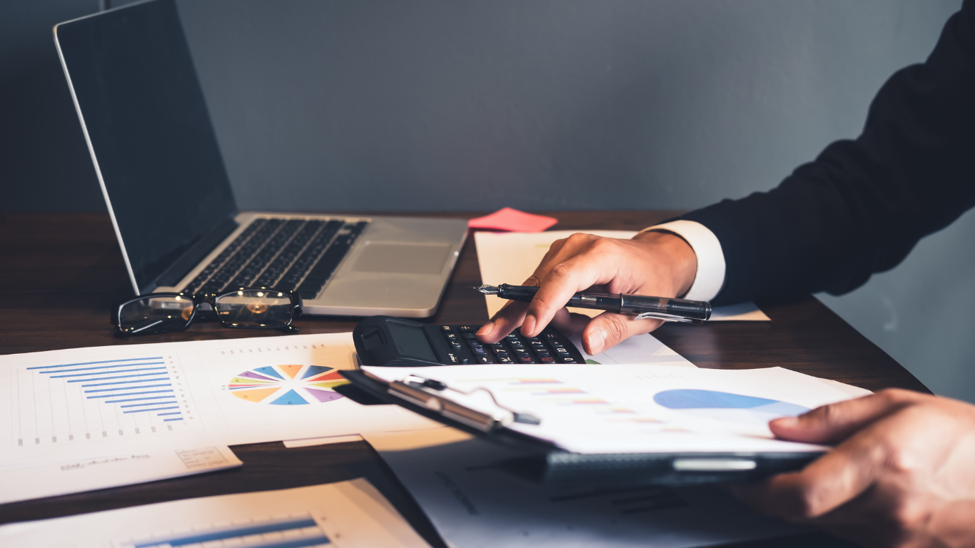 A man is sitting at a desk using a laptop and a calculator.