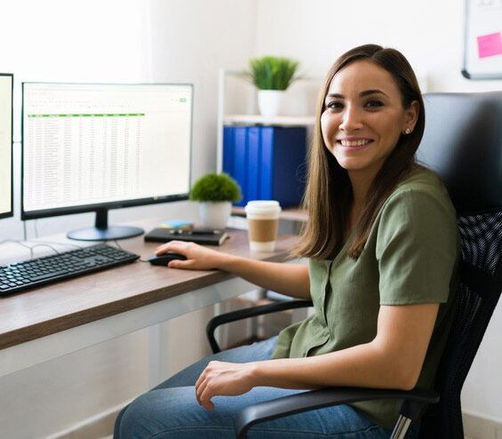 A woman is sitting in an office chair in front of a computer.