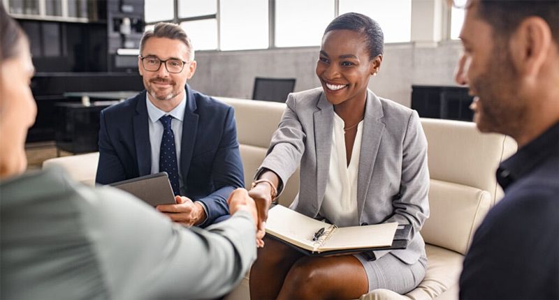 A group of business people are shaking hands while sitting on a couch.
