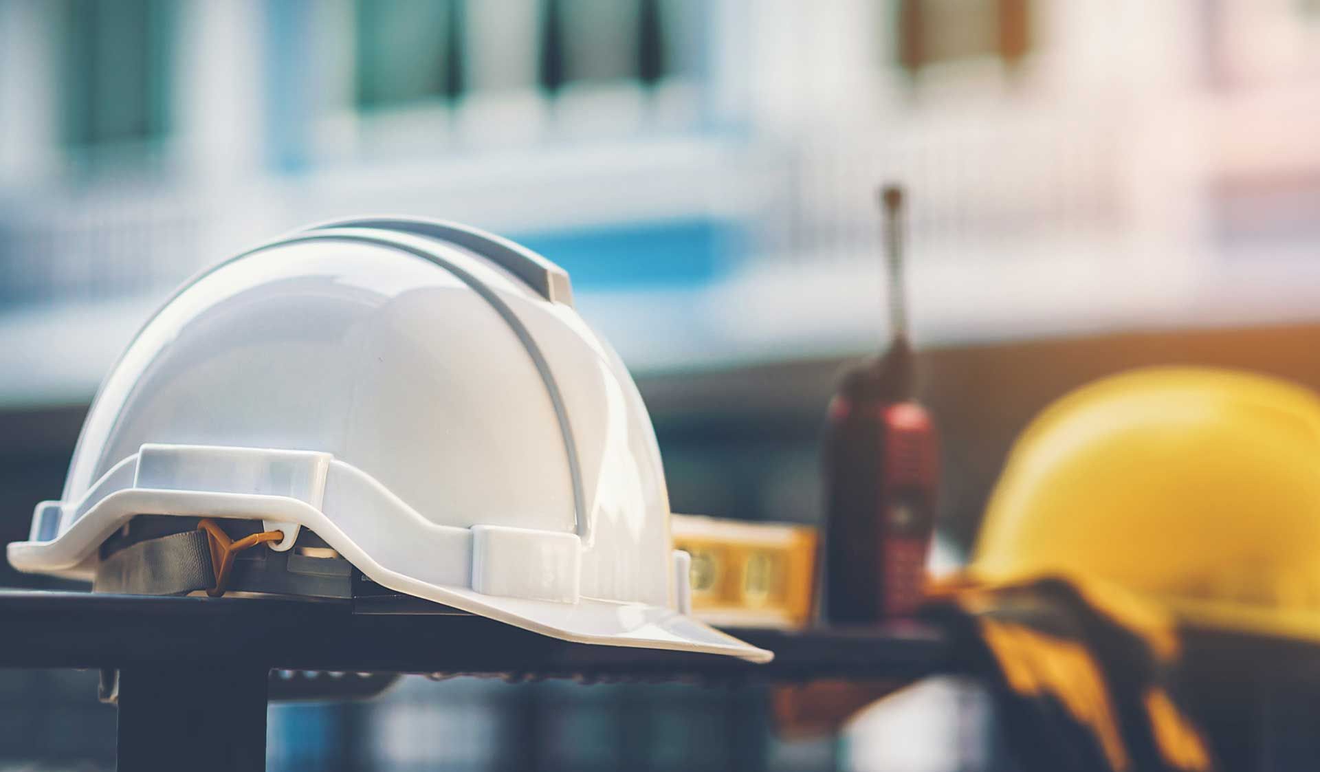 A white hard hat is sitting on a table next to a yellow hard hat.