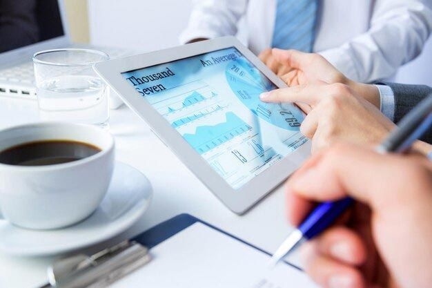 A group of people are looking at a tablet with a cup of coffee on the table.