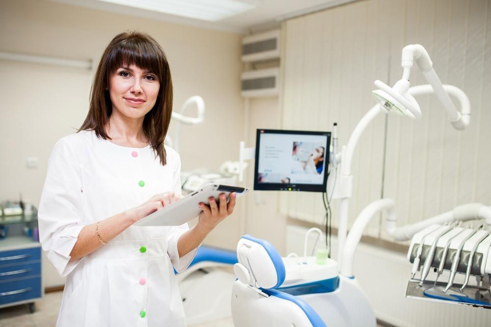 A female dentist is standing in a dental office holding a clipboard.