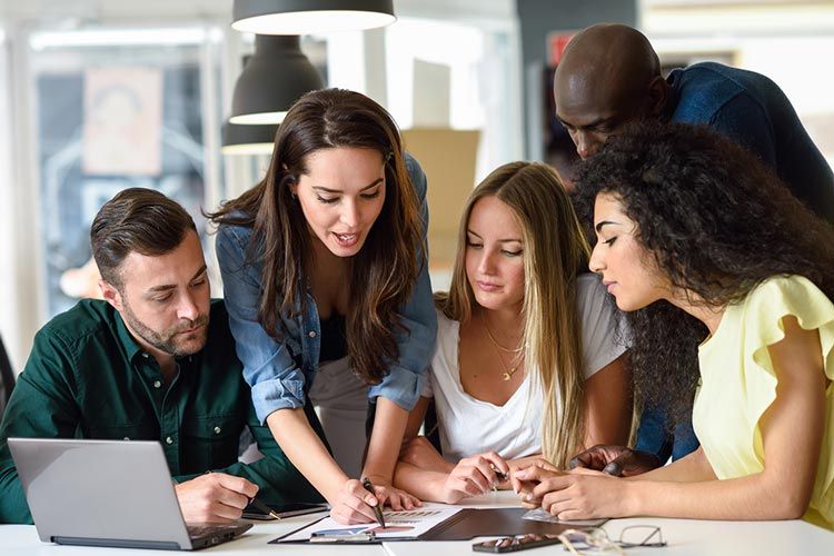 A group of people are sitting around a table looking at a laptop.