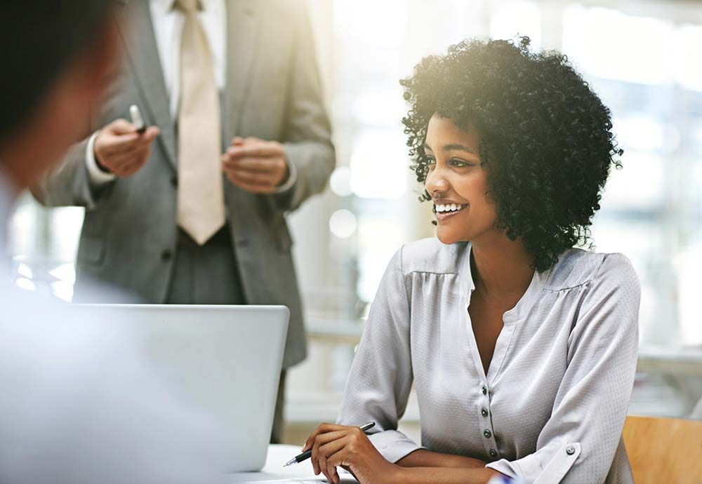 A woman is sitting at a table with a laptop and a man is standing behind her.