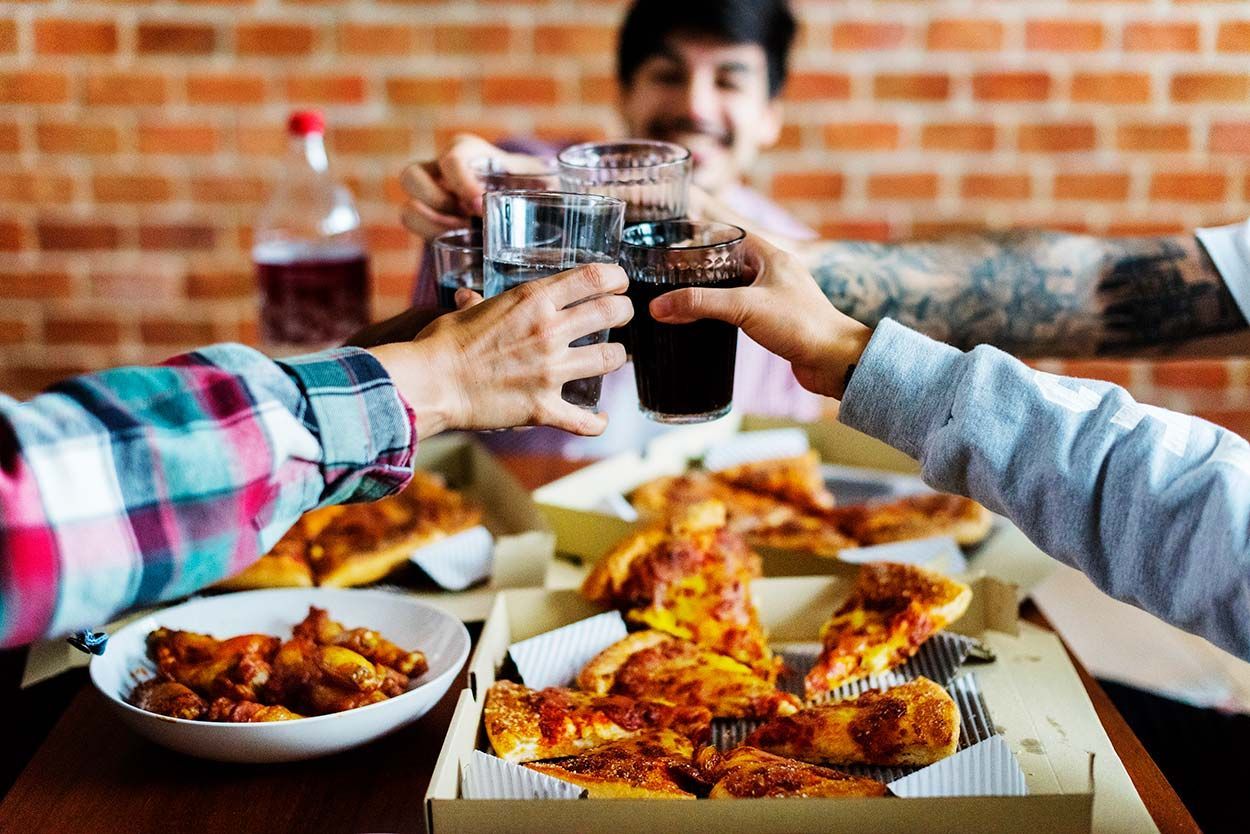 A group of people are sitting at a table eating pizza and drinking soda.